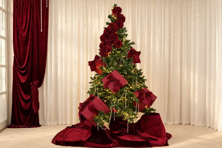 Albero di Natale con rose e pacchi in velluto bordeaux davanti a tende chiare