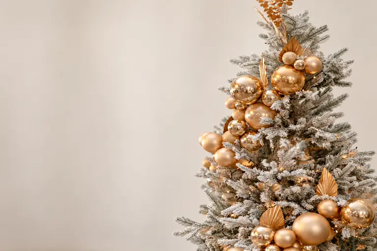 Dettaglio di albero di Natale innevato con sfere oro champagne su fondo crema