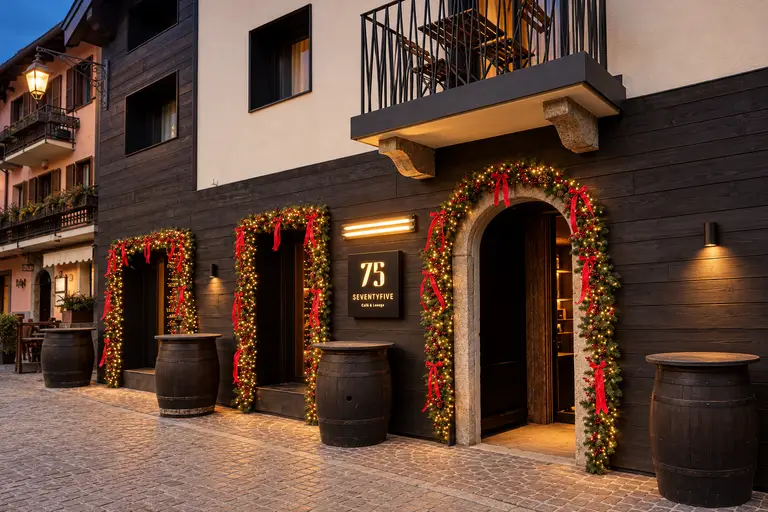 Facciata di un locale con tre ingressi decorati da ghirlande natalizie luminose e fiocchi rossi, al crepuscolo